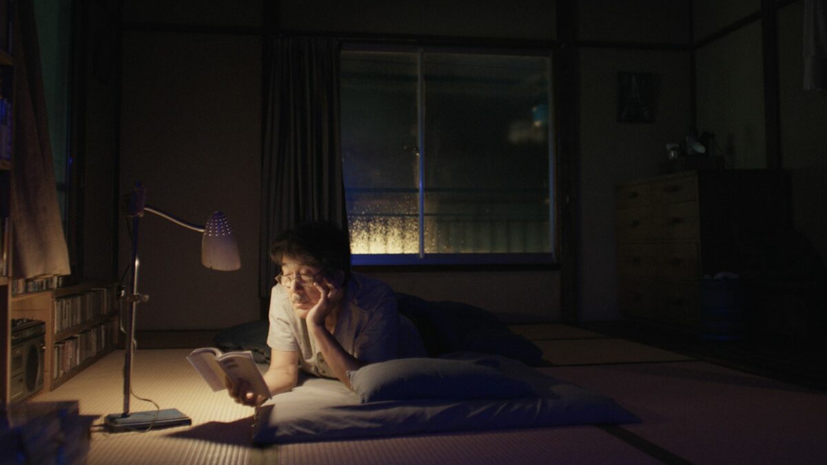 Mężczyzna czytający książkę na łóżku przy nocnej lampce.