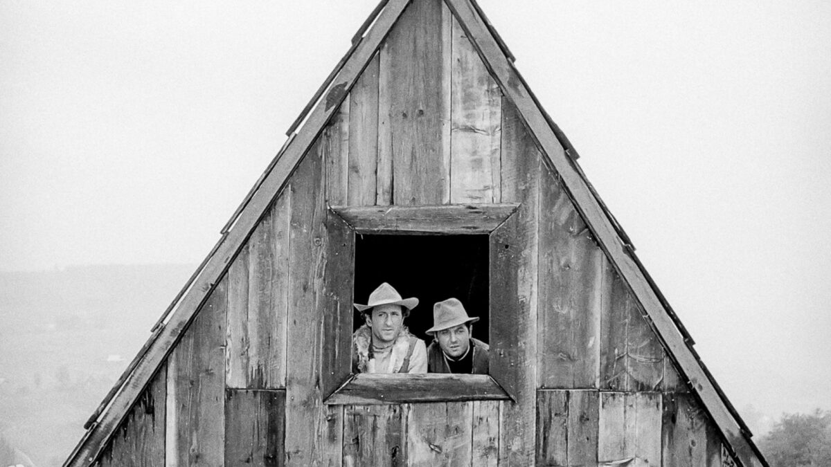 Dwójka mężczyzn wygląda przez okno z wiejskiej chaty.