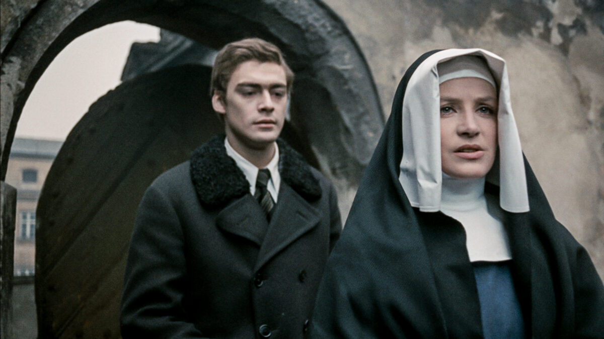 Zakonnica prowadzi mężczyznę do bramy wejściowej.