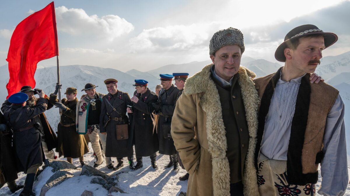 Górale na szczycie góry, za nimi niemieccy żołnierze wbijają nazistowską flagę.