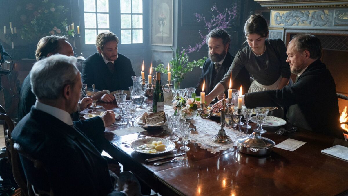 Kobieta podająca wystawną kolację, przy stole grupa mężczyzn.