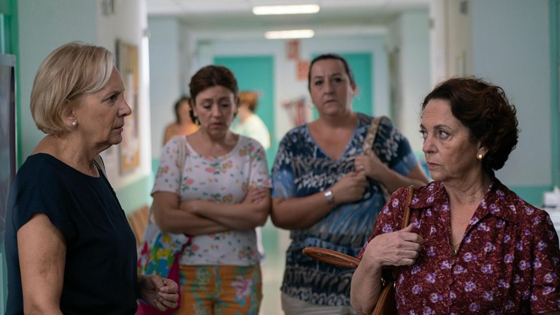 Cztery kobiety prowadzące rozmowę w szpitalnym korytarzu.