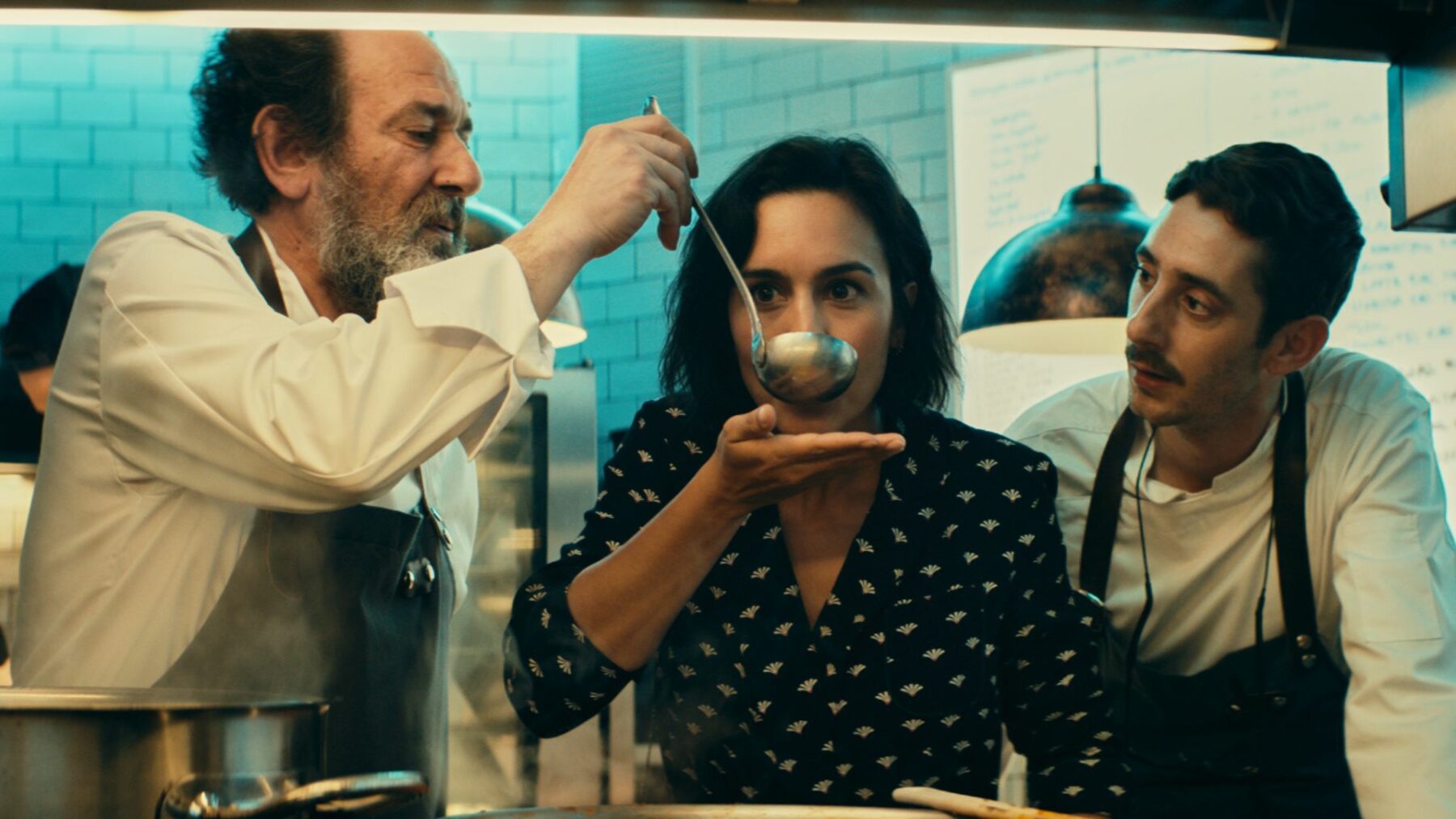 Kadr przedstawia dwóch kucharzy i kobietę pośrodku próbująca potrawę.