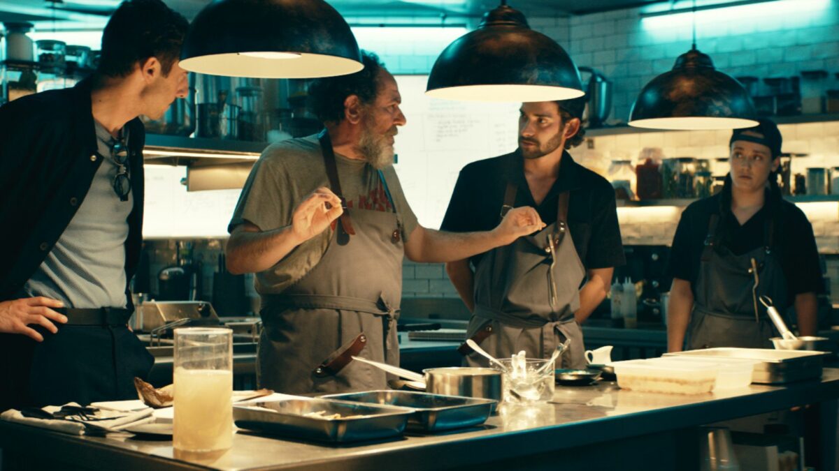 Grupa mężczyzn przy kuchennym blacie prowadzi ożywioną rozmowę.