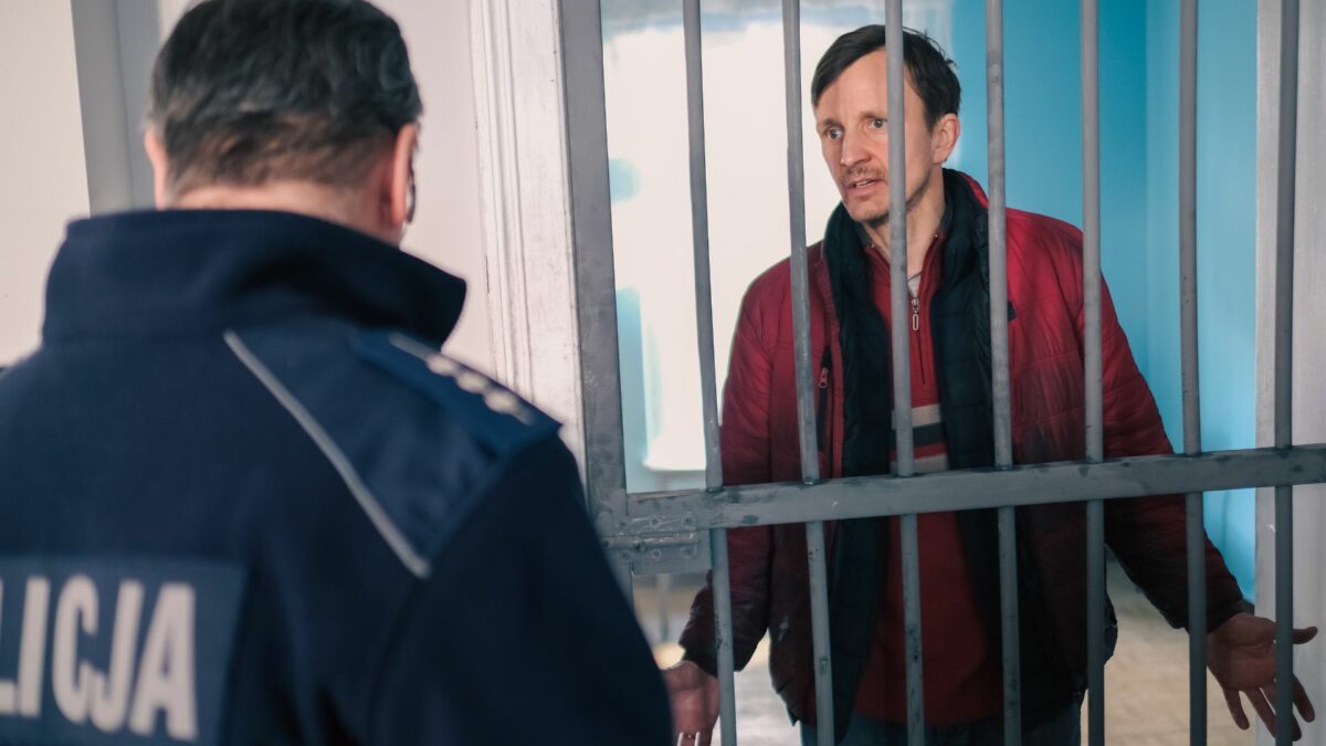 Mężczyzna w areszcie próbujący porozmawiać z policjantem.