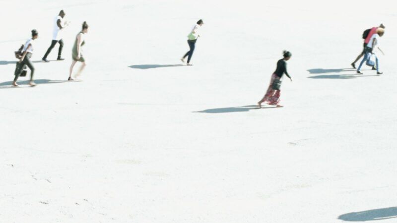 Grupa ludzi przemieszcza się po jasnym gruncie rzucając za sobą cień