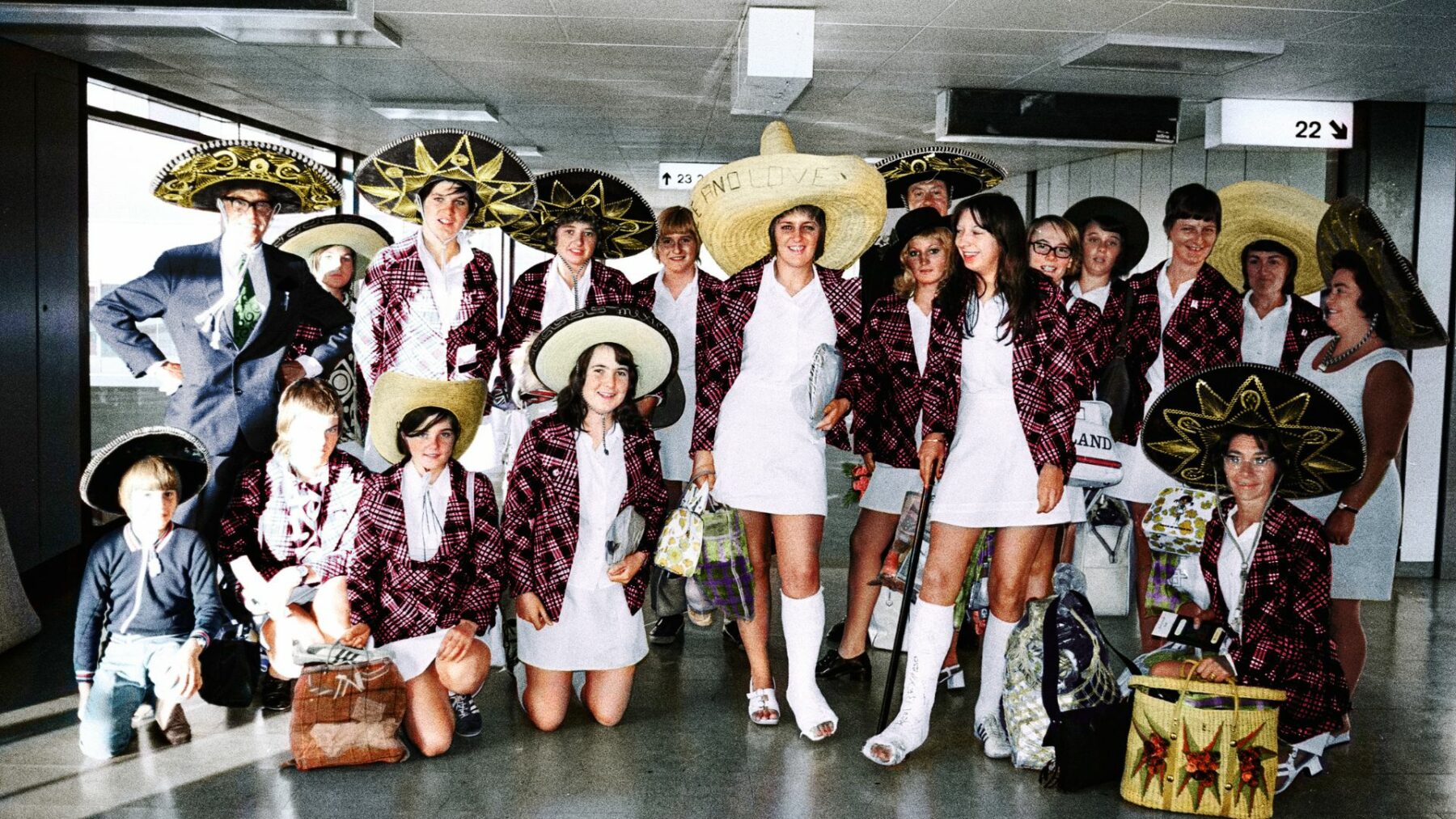Zdjęcie grupy piłkarek na lotnisku, z czego niektóre z nich mają na głowie meksykańskie kapelusze, a dwie mają nogę w gipsie