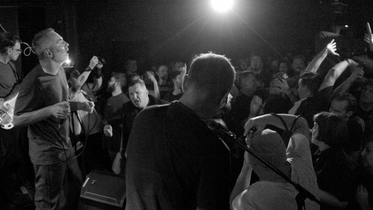 Czarno-biały kadr z muzykami grającymi koncert oraz tańczącą publicznością