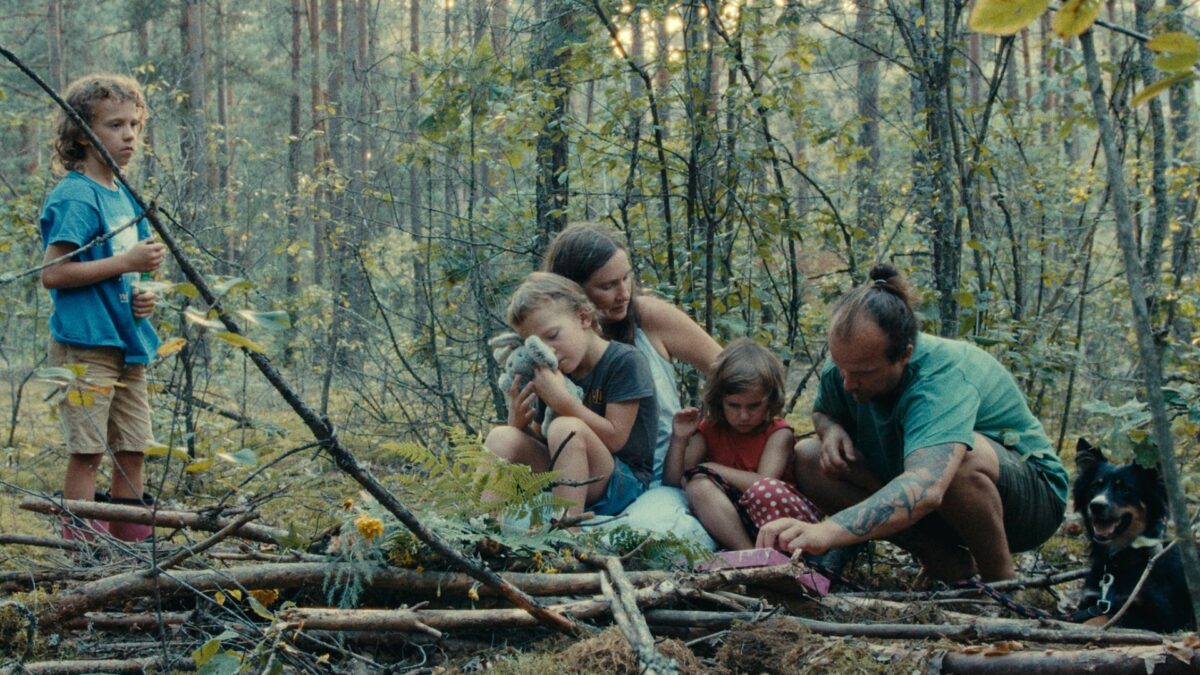Dorosły mężczyzna i kobieta z trójką dzieci oraz psem przesiadują w lesie