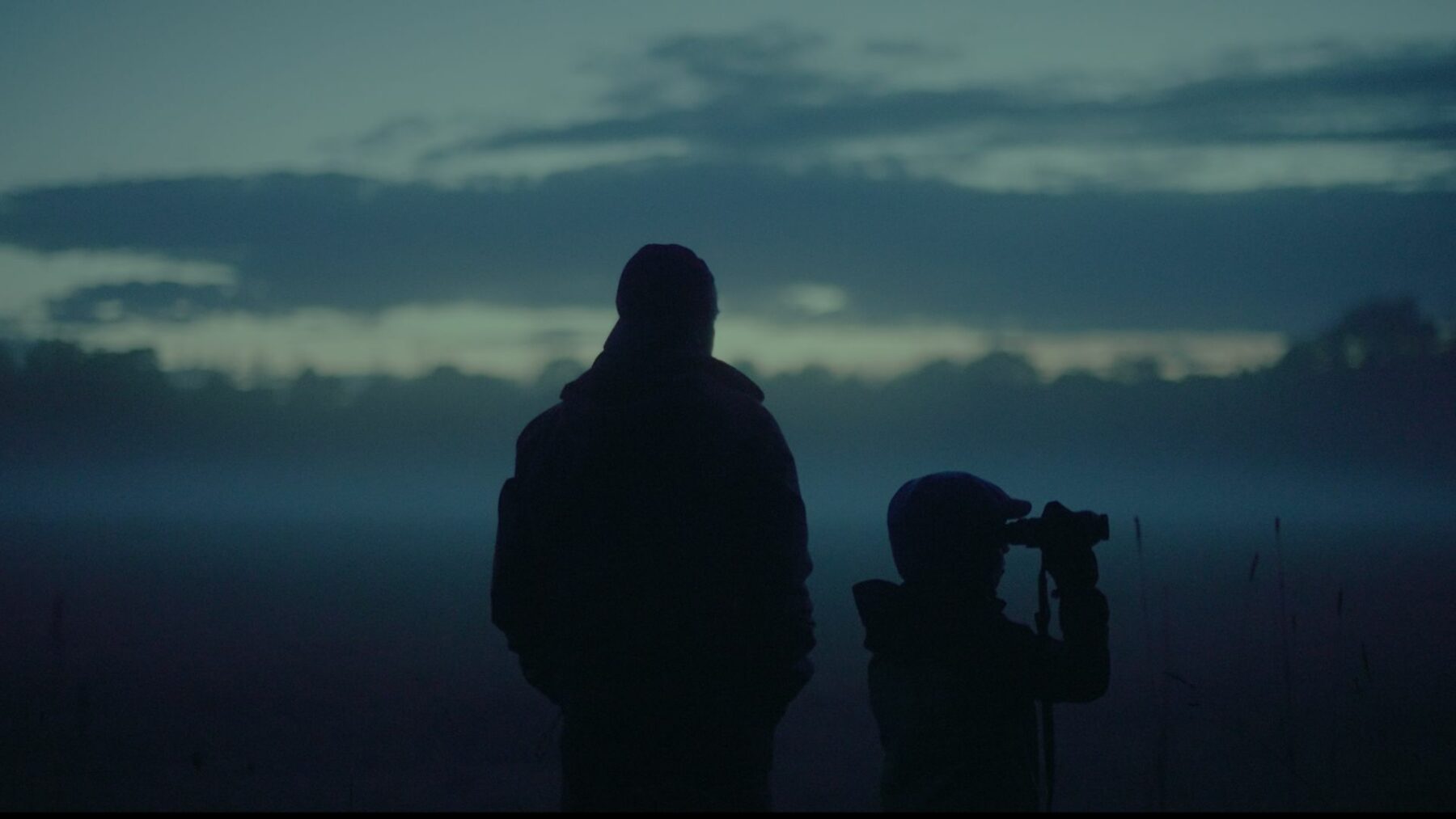 Sylwetka dorosłego mężczyzny i dziecka z lornetką na tle osnutego mgłą krajobrazu