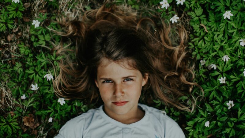 Dziewczynka leży otoczona kwiatami na ściółce leśnej