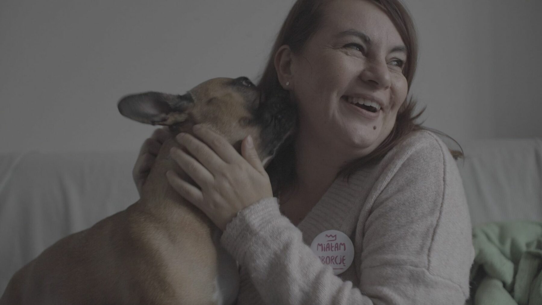 Kobieta z przypinką "Miałam aborcję" na piersi przytula liżącego ją psa