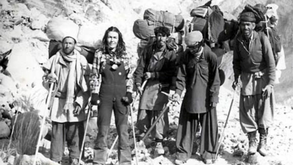 Czarno-biały kadr z kobietą poruszającą się o kulach i czterema mężczyznami z dużymi plecakami