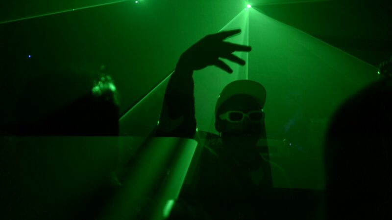 Mężczyzna w czapce z daszkiem i okularach przeciwsłonecznych tańczy w zielonym świetle