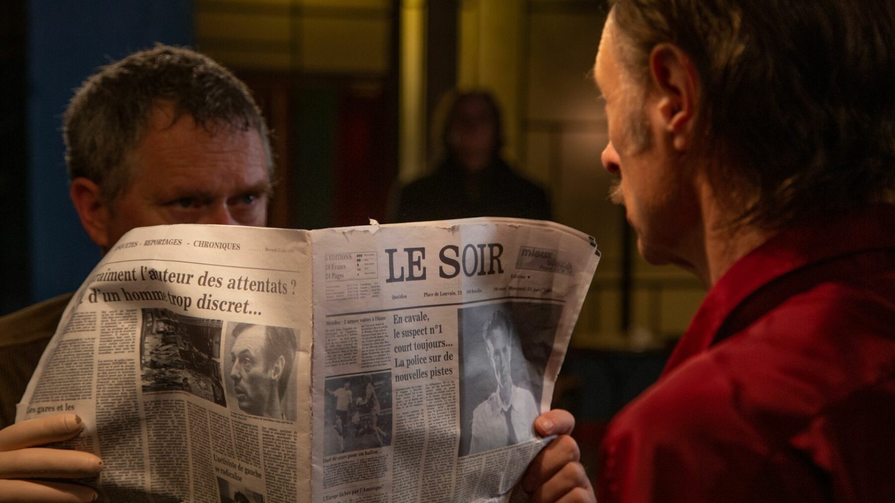 Kadr przedstawia mężczyznę chowającego twarz za gazeta.