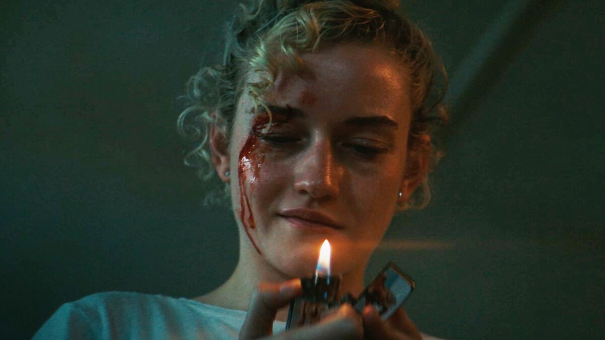 Zakrwawiona dziewczyna wpatruje się w ogień od zapalniczki.