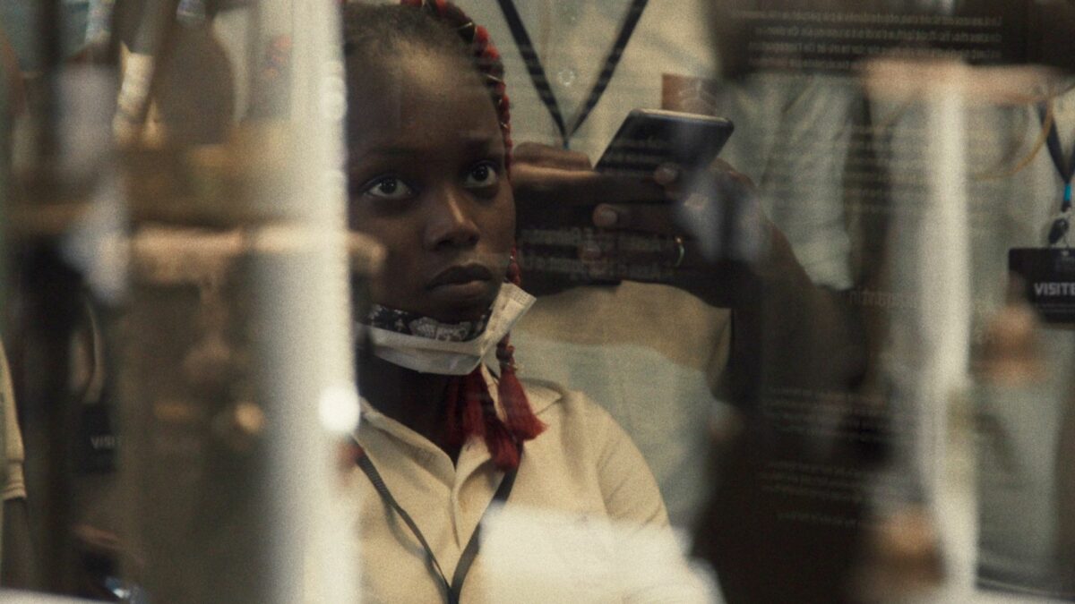 Kadr ze spojrzeniem na młodą dziewczynę zza gabloty muzealnej.