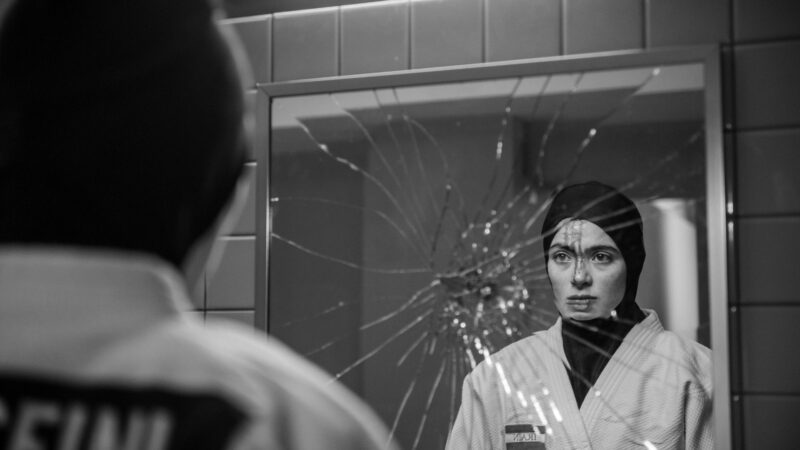 Kobieta w stroju sportowym stoi przed rozbitym lustrem.