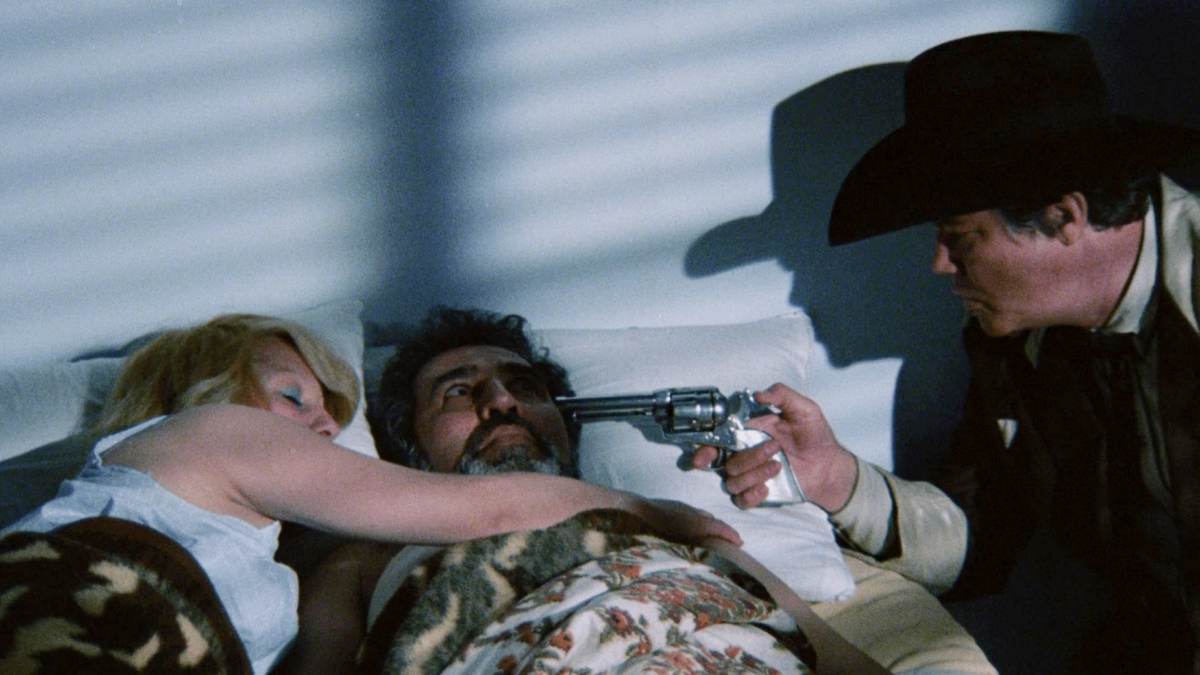 Mężczyzna celuje z broni do pary śpiącej w łóżku.