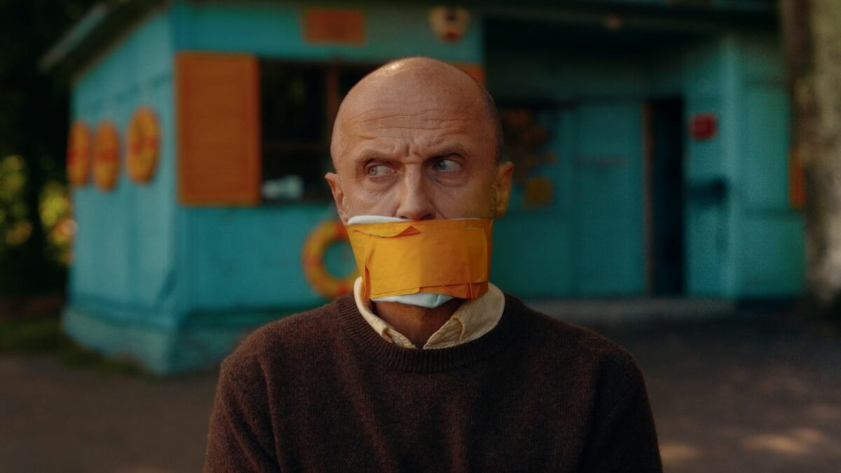 Zbliżenie na zaiązanegi i zakneblowanego mężczyznę.