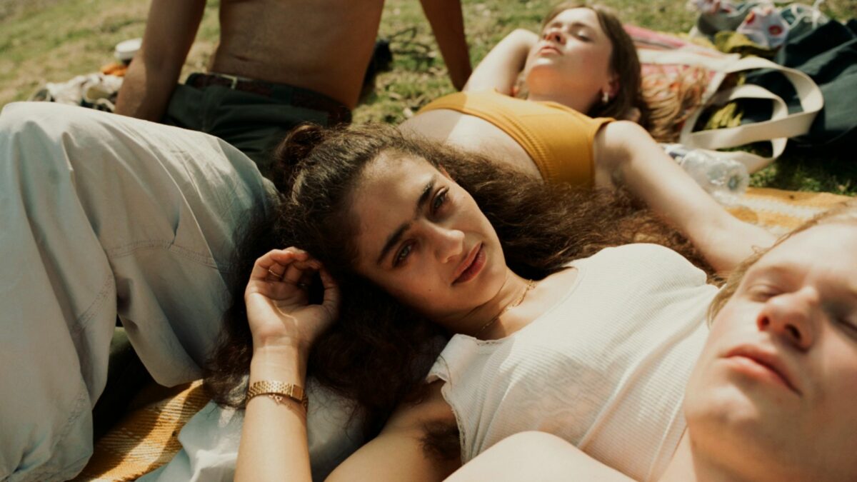 Grupa młodych ludzi odpoczywających na kocu nad wodą.