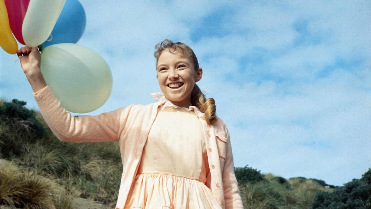 Dziewczynaka biegnąca na dworze z balonami trzymanymi na sznurku.