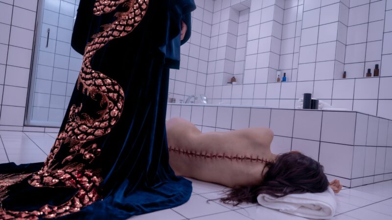 Naga kobieta leżąca na podlodze z dużymi ranami wzdłuż kręgosłupa.