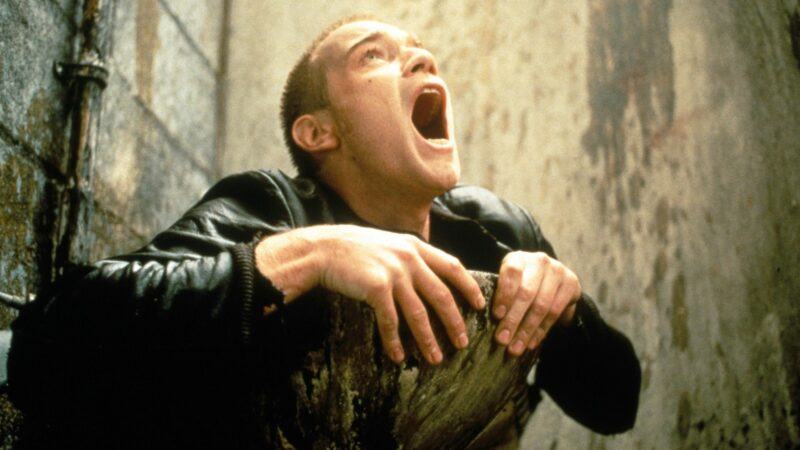 Kadr z publicznej toalety przedstawia mężczyznę próbującego wydostać się z muszli klozetowej.