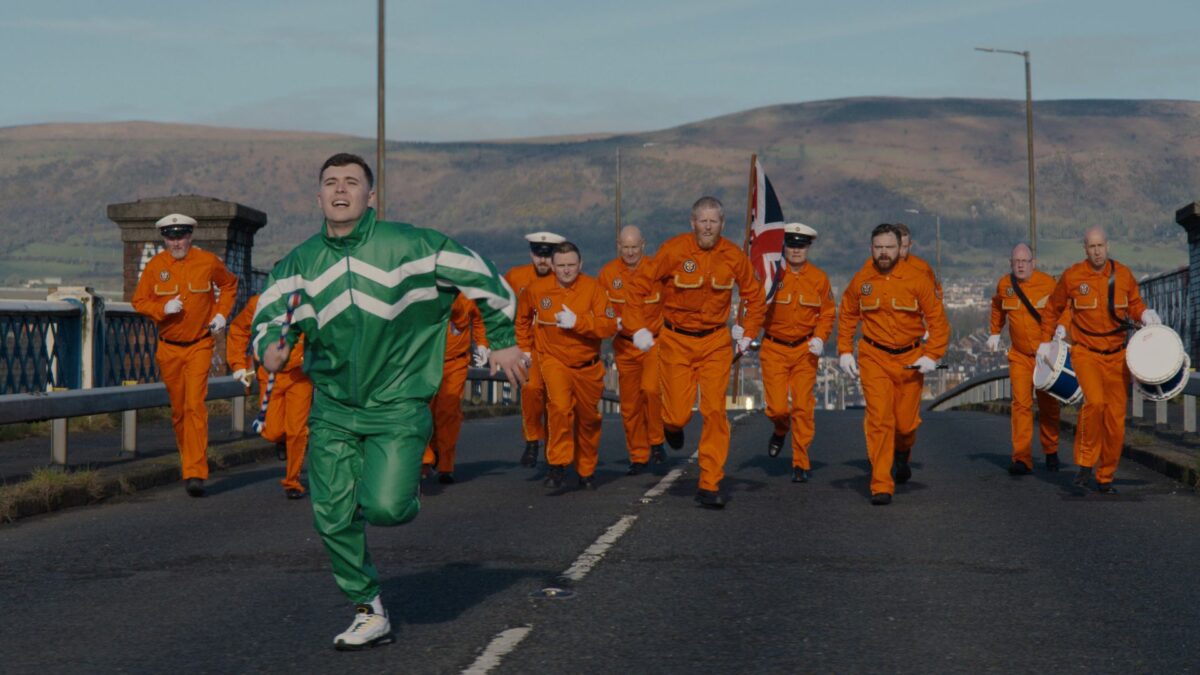 Chłopak w zielonym dresie ucieka przed grupą mężczyzn.