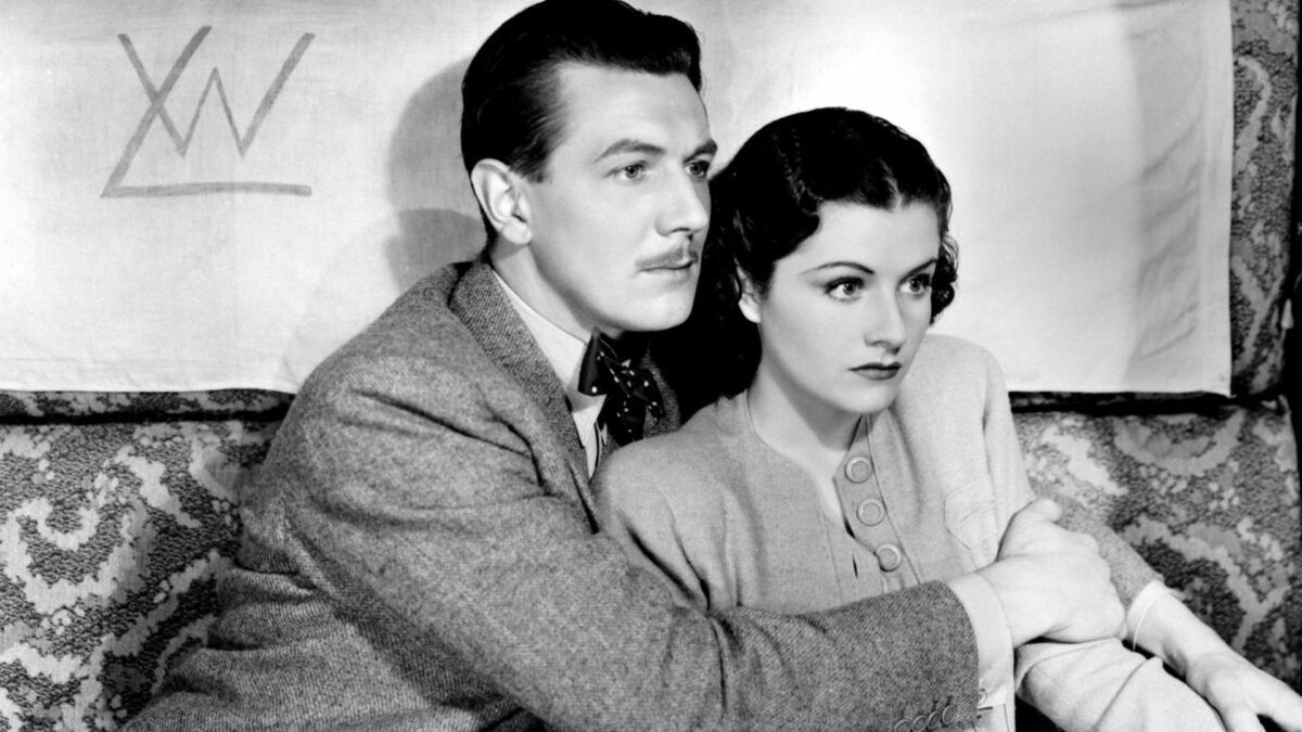 Para ubrana w stylu lat trzydziestych. Mężczyzna obejmuje kobietę. Obydwoje wyglądają na przestraszonych.