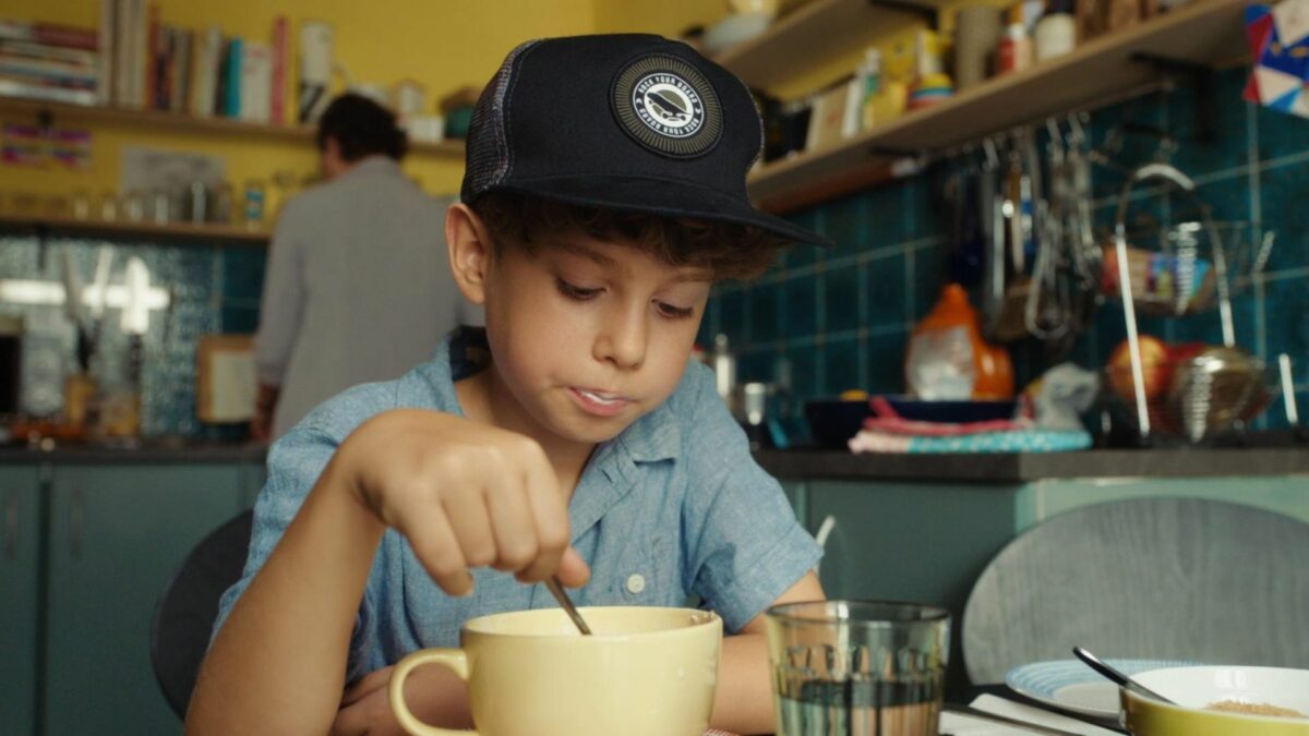 Chłopczyk w czapce z daszkiem pije mleko przy kuchennym stole.