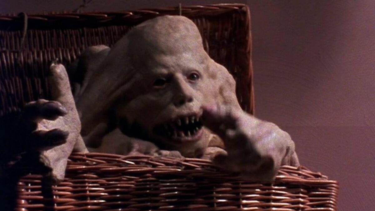 Duży wiklinowy koszyk a w nim zniekształcona ludzka postać.