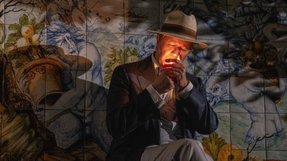 Starszy mężczyzna w kapeluszu odpala papierosa.