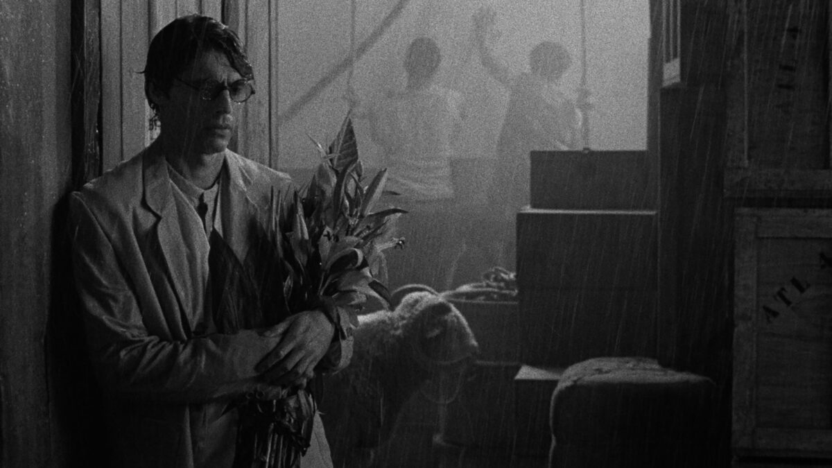 Przemoczony od deszczu mężczyzna z bukietem kwiatów w dłoniach.