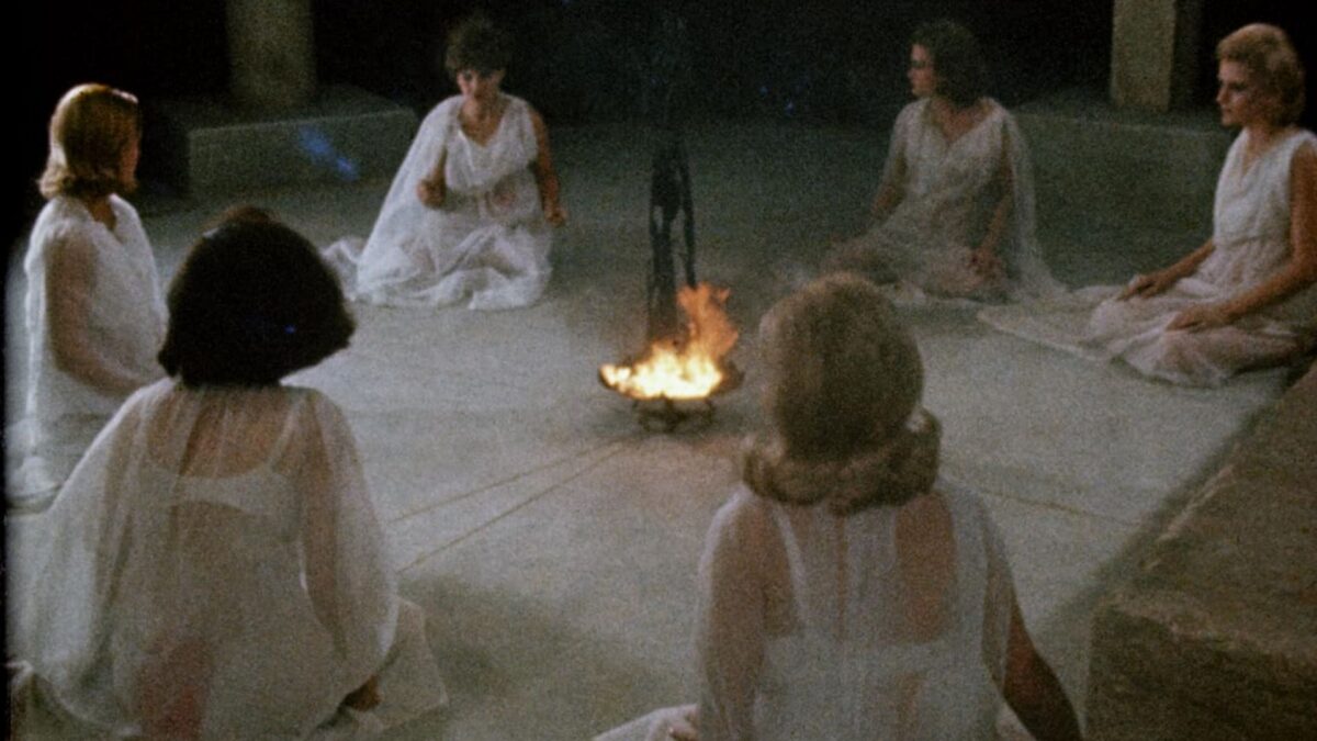 Kobiety w białych sukienkach siedzące w kręgu przed ogniskiem.