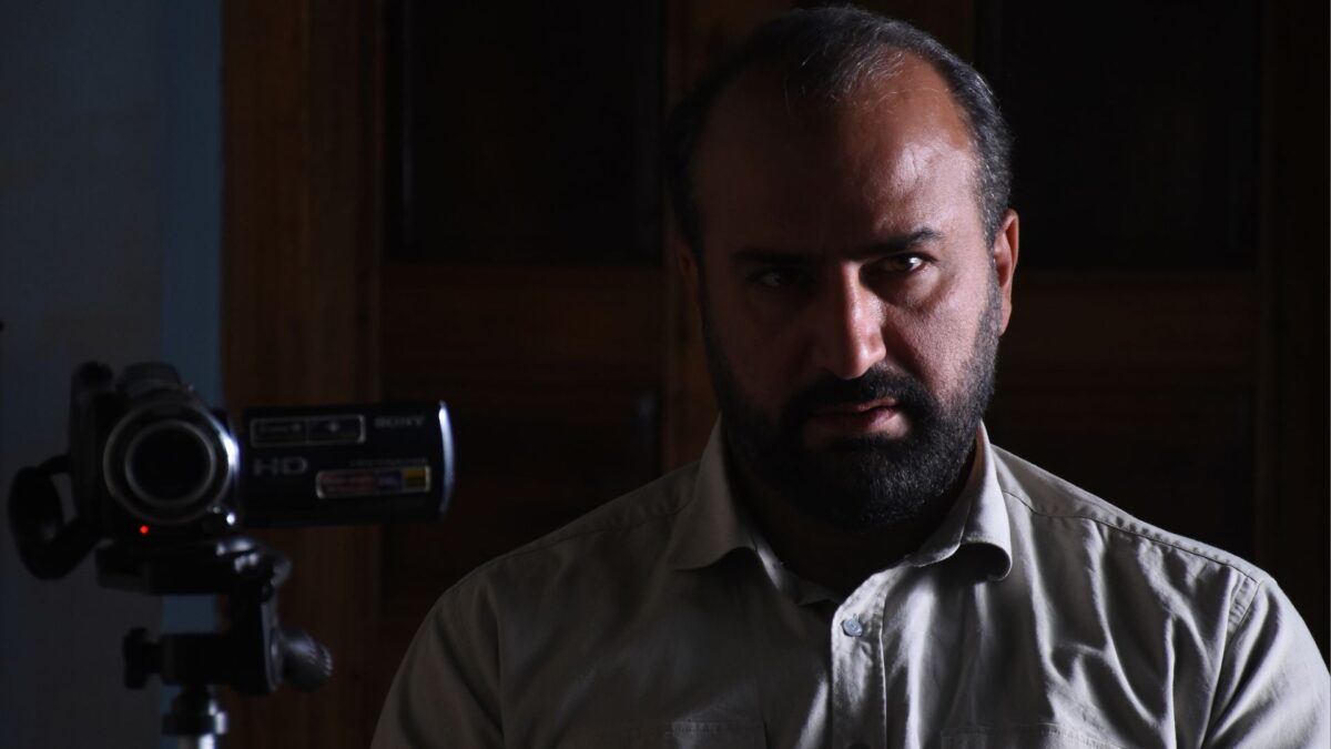 Zbliżenie na mężczyzne a obok niego kamera na statywie.