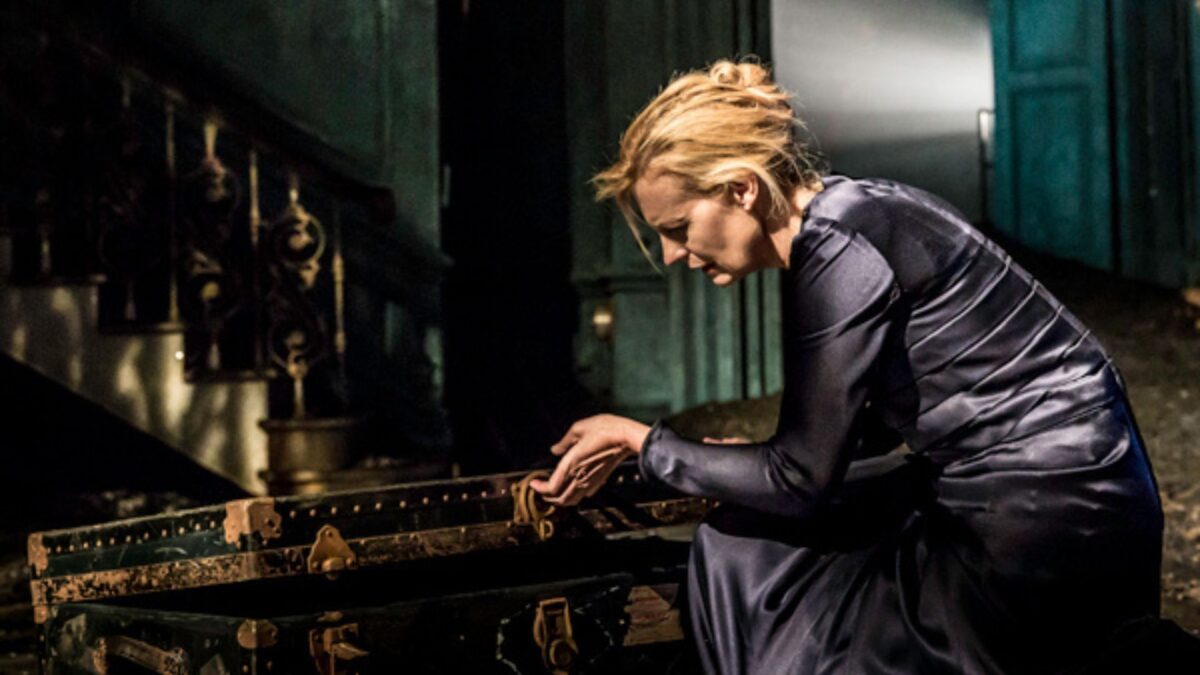 Kadr ze sceny teatralnej a na niej aktorka przy stole.