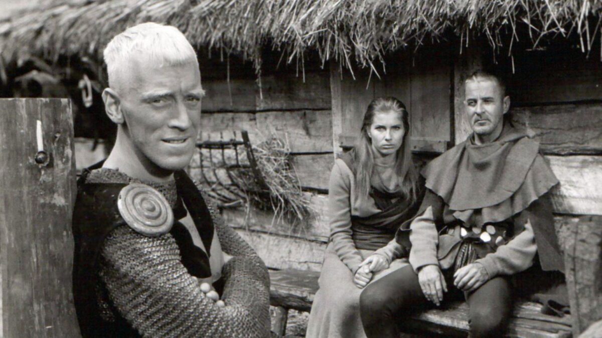 Grupka ludzi przed średniowiecznej chatce.