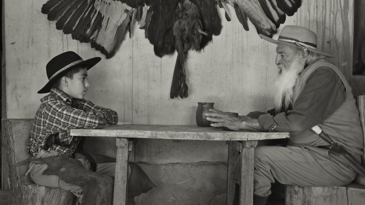 Dziadek siedzi razem ze swoim wnukiem przy stole.