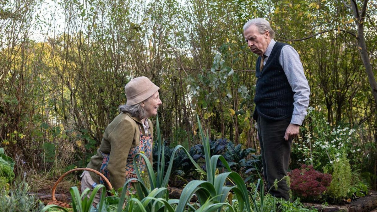 Staruszek obserwuje swoją żonę pracującą w ogrodzie.