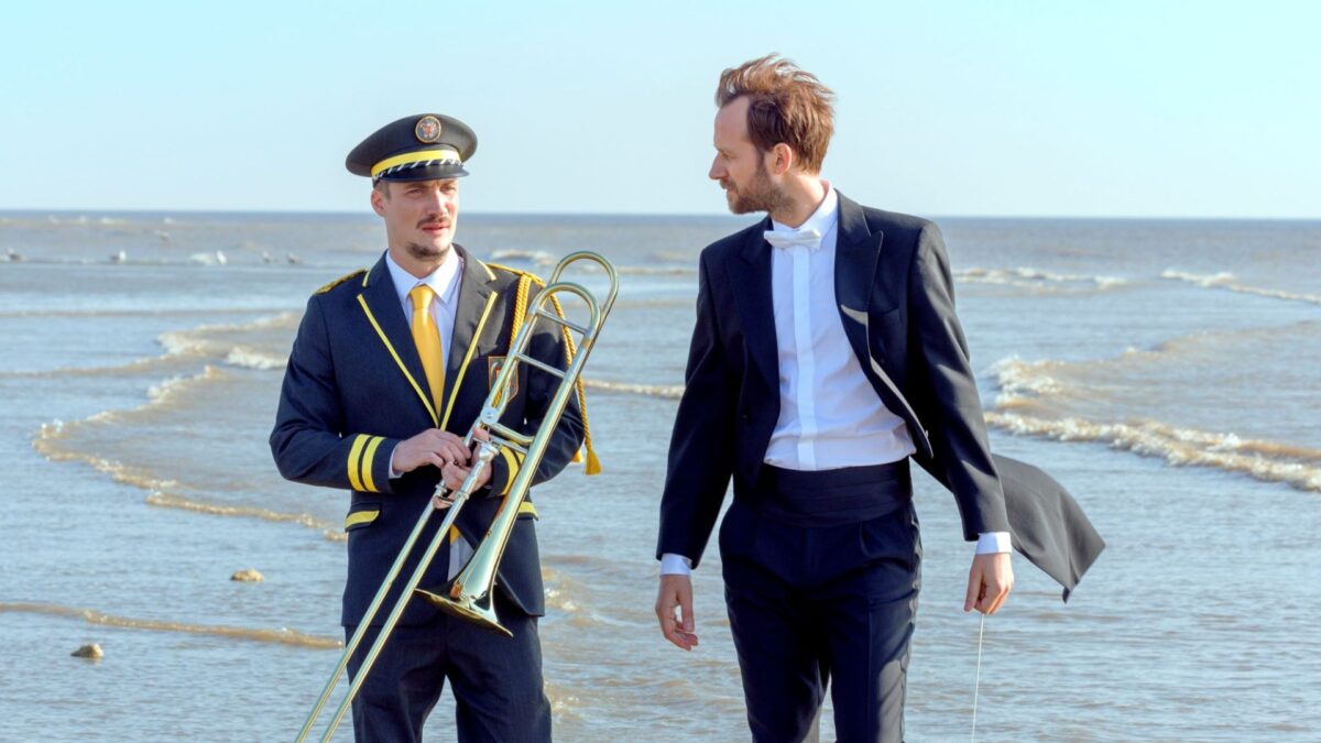 Mężczyzna w garniturze w towarzystwie muzyka na plaży.