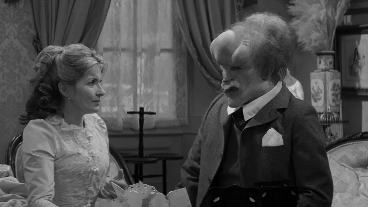 Zdeformowany mężczyzna rozmawia z młodą kobietą.